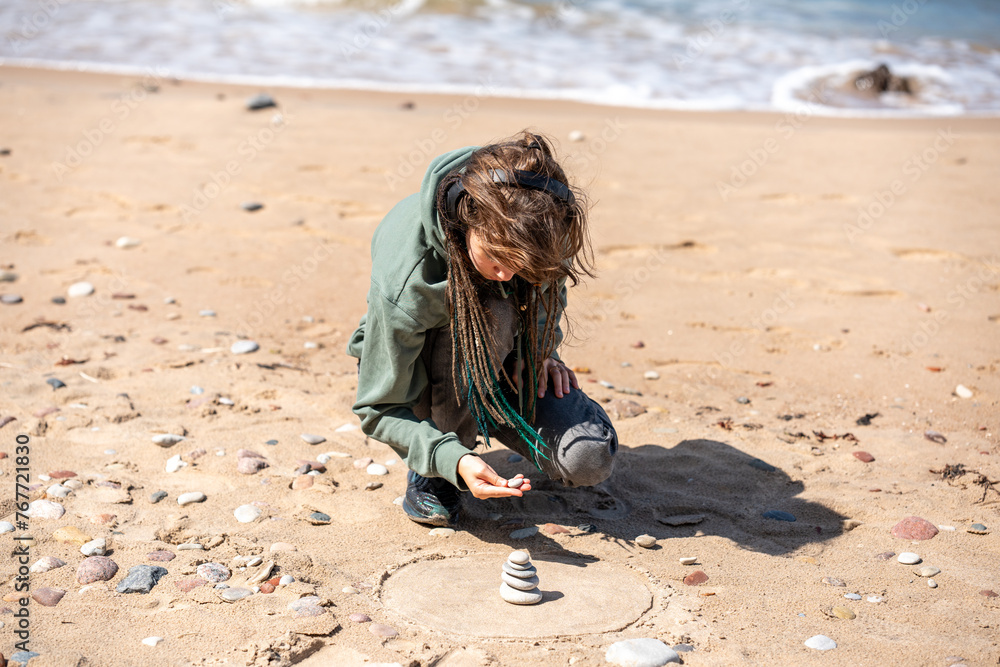 Alone teenager girl in green hoodie stacking stones on the Baltics seashore. Alone teenager girl in green hoodie stacking stones on the Baltics seashore.