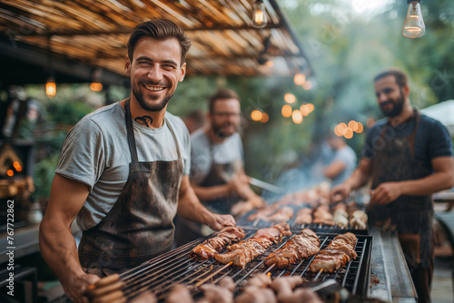 Group of smiling men cooking meat on the grill at an outdoor barbecue party, having fun together. Barbecue event with men cooking meat on the grill outdoors. photo