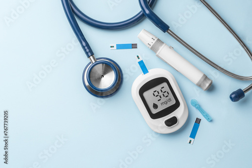 Blood glucose meter, lancet and stethoscope on blue background, top view