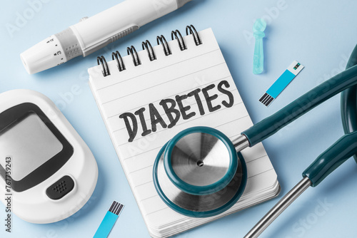 Diabetes word on notepad with glucometer, lancet and stethoscope on blue background