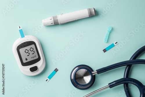 Diabetes concept with glucometer, lancet and stethoscope on green background, top view
