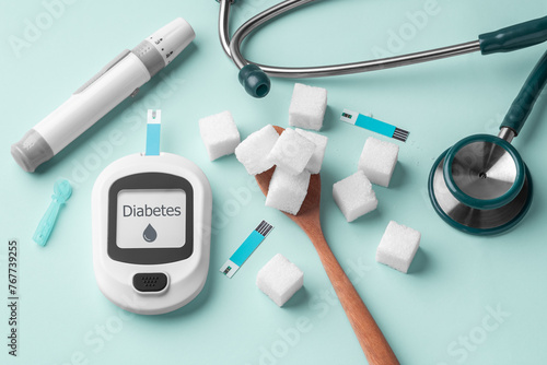 Diabetes concept with blood glucose meter and sugar cube on spoon on green background