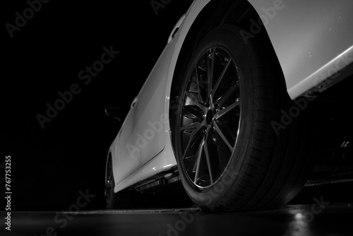 Low angle, back, rear view of white long car, luxury  new vehicle and its tires at the repairing shop. Concept of car maintenance service. empty Copy space. isolated on black background. night scene.