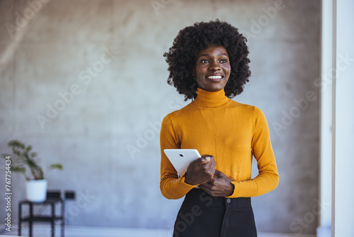 Half length portrait of african american female leader of working team standing on frontage while her colleagues talking on background prosperous business woman in casual wear looking at camera photo