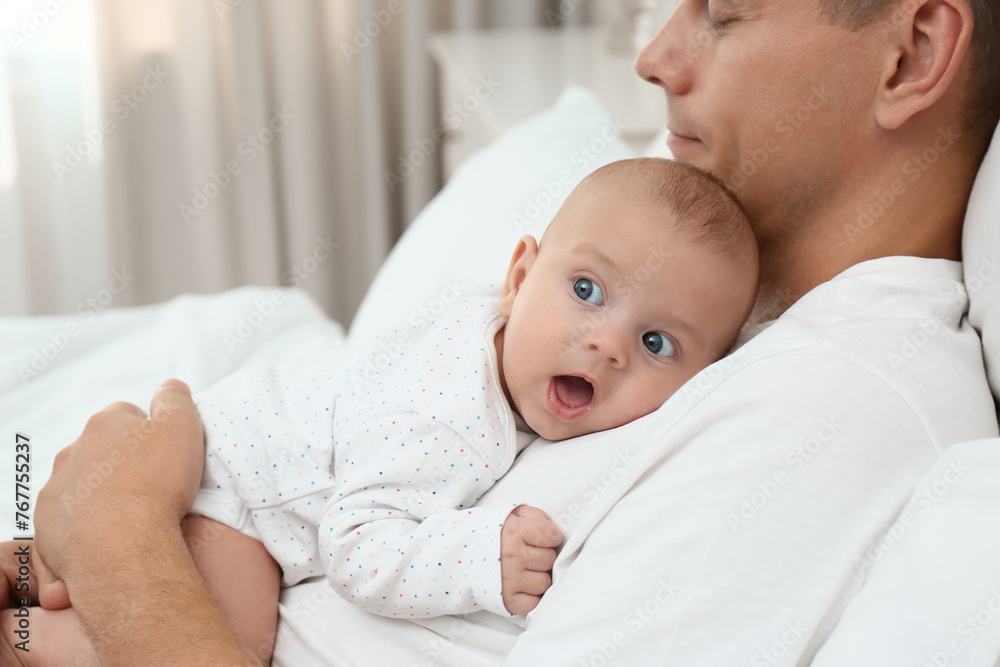 Father holding his cute baby on bed at home, closeup Father holding his cute baby on bed at home, closeup