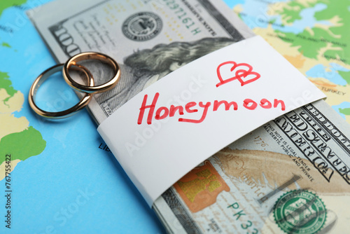Two golden rings and stack of money with word Honeymoon on world map, closeup