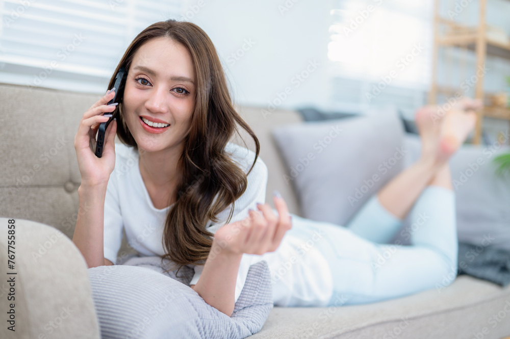 A radiant young woman enjoys a lively conversation on her phone, comfortably lounging on a sofa in a living room. A radiant young woman enjoys a lively conversation on her phone, comfortably lounging on a sofa in a living room.
