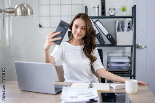 A young woman takes a break for a selfie, in a home office setup with a laptop and documents.