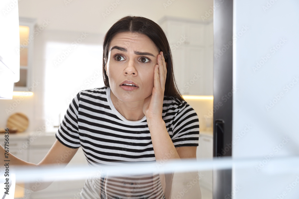 Upset woman near empty refrigerator in kitchen, view from inside Upset woman near empty refrigerator in kitchen, view from inside