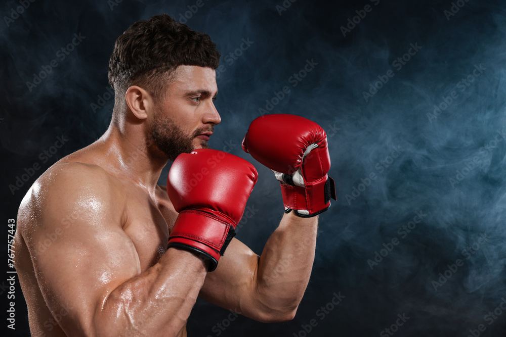 Man wearing boxing gloves fighting in smoke on black background. Space for text