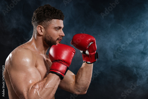 Man wearing boxing gloves fighting in smoke on black background. Space for text © New Africa