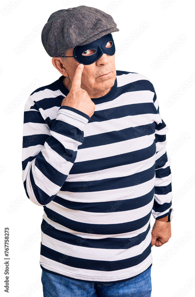 Senior handsome man wearing burglar mask and t-shirt pointing to the eye watching you gesture, suspicious expression Senior handsome man wearing burglar mask and t-shirt pointing to the eye watching you gesture, suspicious expression