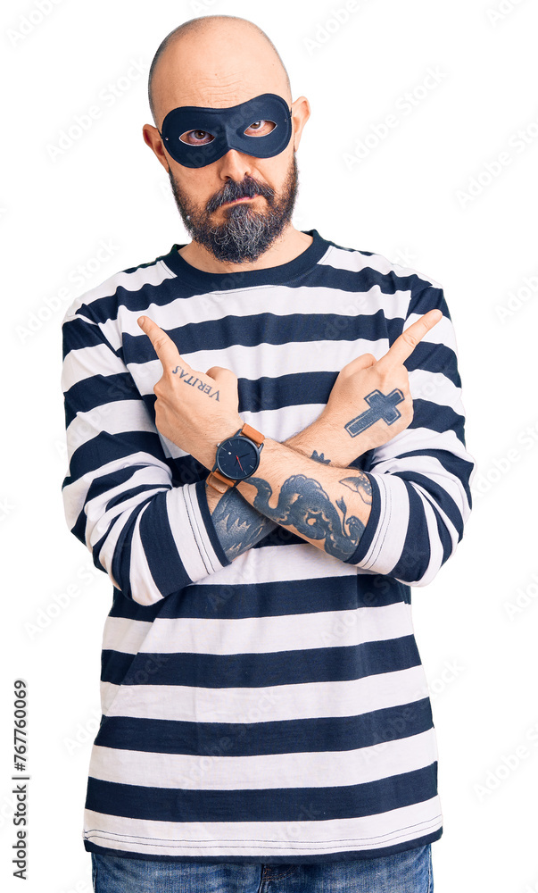 Young handsome man wearing burglar mask pointing to both sides with fingers, different direction disagree Young handsome man wearing burglar mask pointing to both sides with fingers, different direction disagree