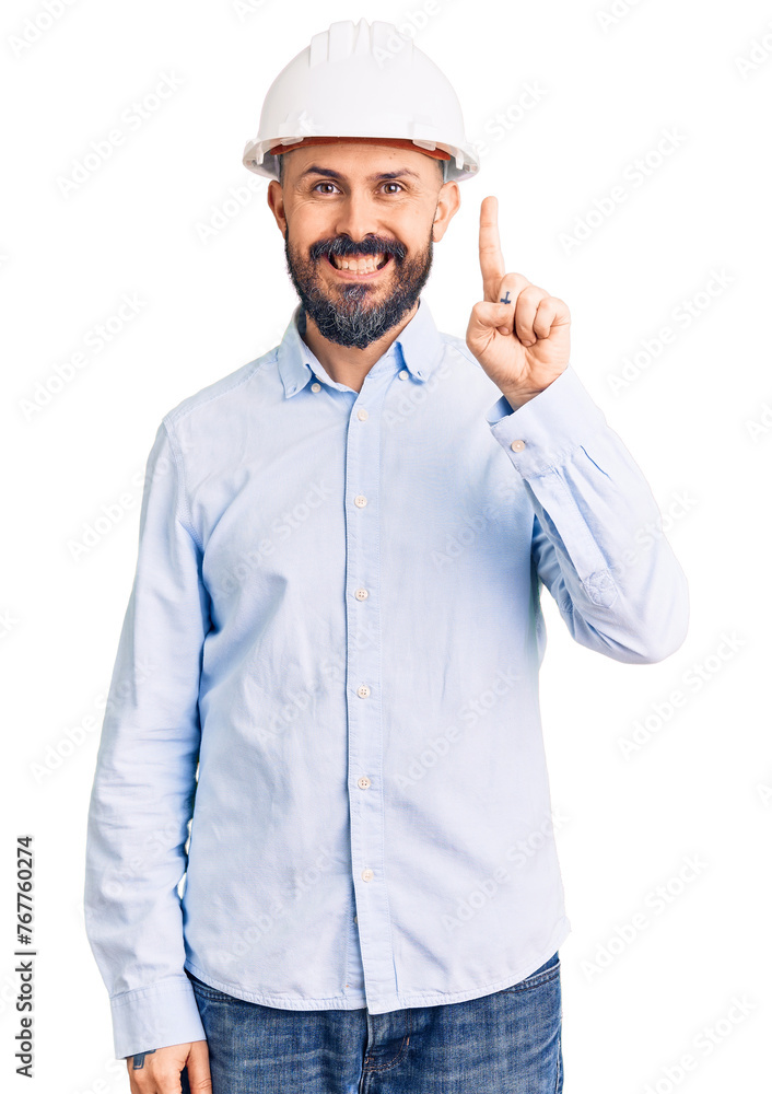 Young handsome man wearing architect hardhat showing and pointing up with finger number one while smiling confident and happy. Young handsome man wearing architect hardhat showing and pointing up with finger number one while smiling confident and happy.