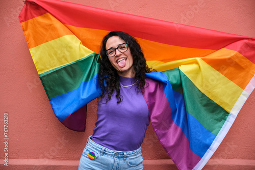 Lesbian woman is holding a rainbow flag and smiling celebrating Pride Month. © Ladanifer