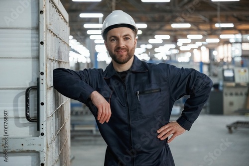 Leaning on the wall. Factory worker is indoors with hard hat © standret