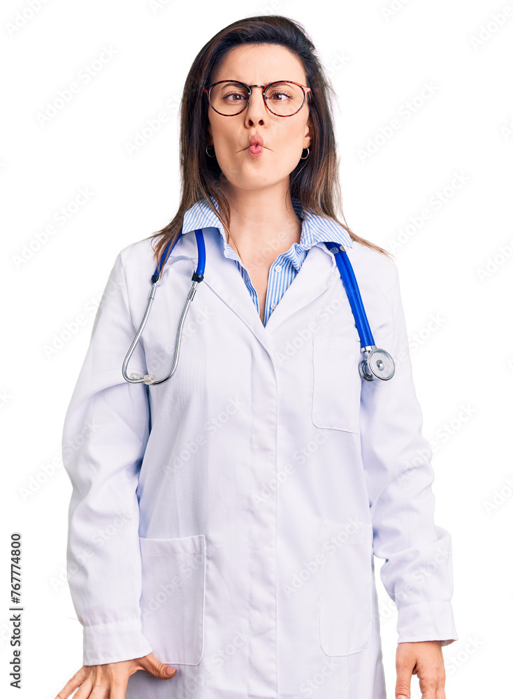 Fototapeta premium Young beautiful woman wearing doctor stethoscope and glasses making fish face with lips, crazy and comical gesture. funny expression.
