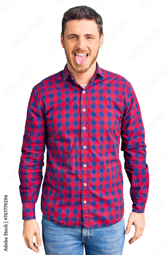 Fototapeta premium Handsome young man with bear wearing casual shirt sticking tongue out happy with funny expression. emotion concept.