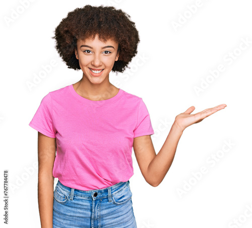 Young hispanic girl wearing casual clothes smiling cheerful presenting and pointing with palm of hand looking at the camera.