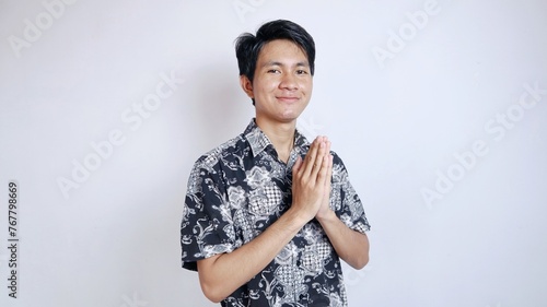 Excited handsome young Asian man dressed in batik with greeting gesture