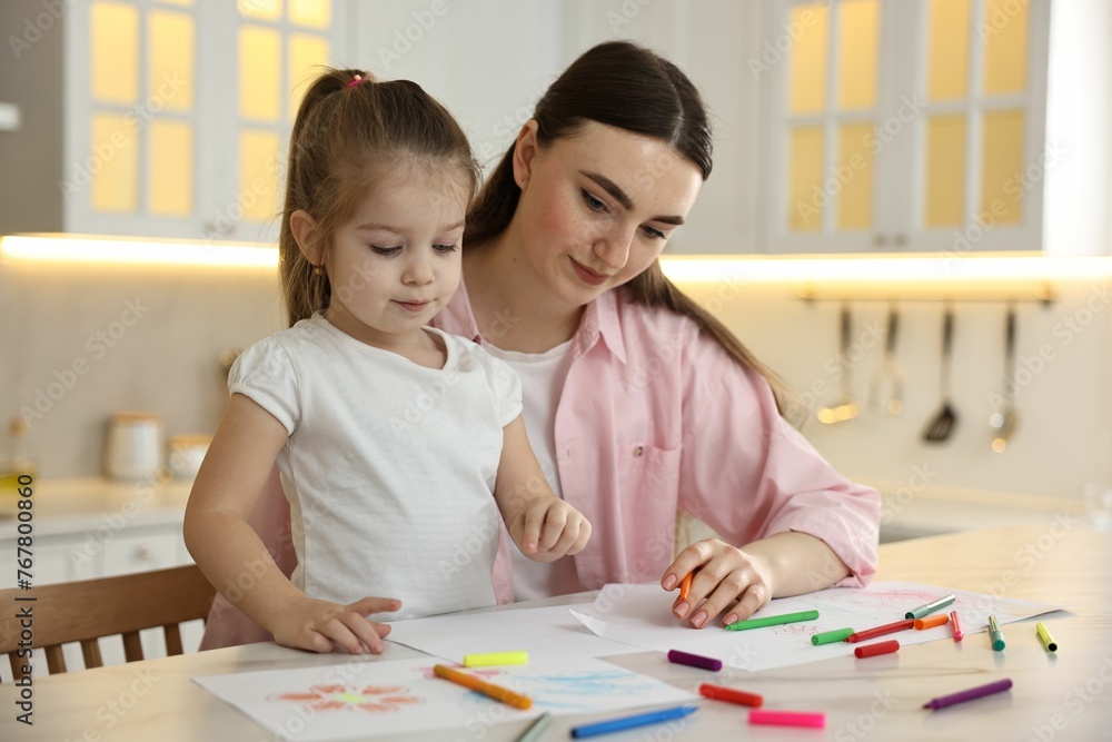 Mother and her little daughter drawing with colorful markers at table in kitchen Mother and her little daughter drawing with colorful markers at table in kitchen
