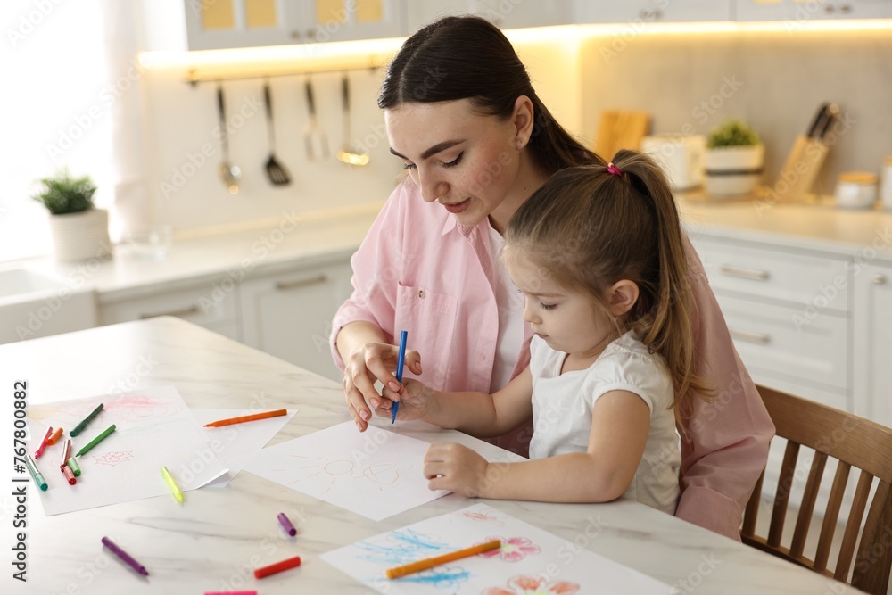 Mother and her little daughter drawing with colorful markers at table in kitchen Mother and her little daughter drawing with colorful markers at table in kitchen