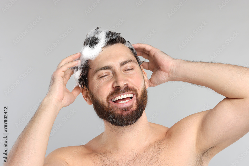 Happy man washing his hair with shampoo on grey background, closeup Happy man washing his hair with shampoo on grey background, closeup