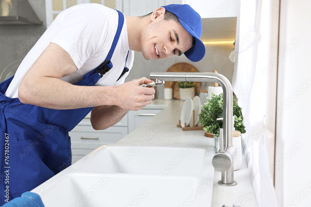 Smiling plumber repairing faucet with spanner in kitchen Smiling plumber repairing faucet with spanner in kitchen