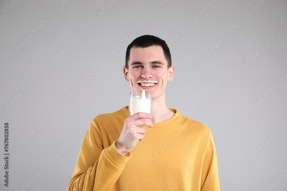 Happy man with milk mustache holding glass of tasty dairy drink on gray background Happy man with milk mustache holding glass of tasty dairy drink on gray background