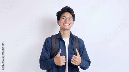 Portrait of young handsome Asian student excited gesturing showing thumbs up on isolated white background