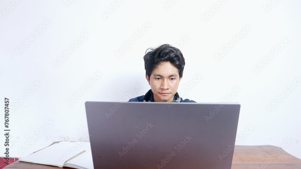 young Asian male student is studying in front of a laptop, doing assignments young Asian male student is studying in front of a laptop, doing assignments