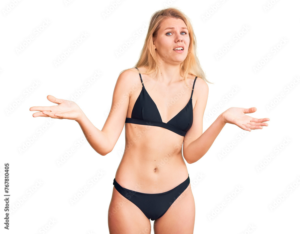 Young beautiful blonde woman wearing bikini clueless and confused with open arms, no idea concept. Young beautiful blonde woman wearing bikini clueless and confused with open arms, no idea concept.