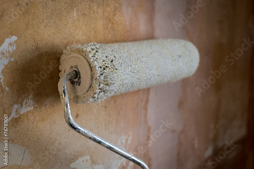 Paint roller extendable pole over rough old concrete wall during home renovation in england uk