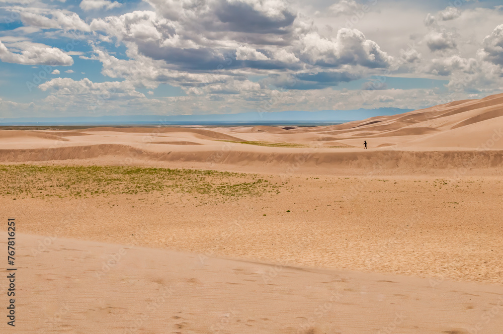 An expansive shot of a single figure contrasting against the magnitude of rolling dunes and a wide sky, depicting solitude