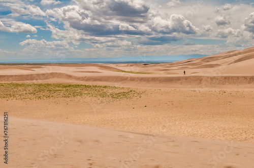 An expansive shot of a single figure contrasting against the magnitude of rolling dunes and a wide sky, depicting solitude