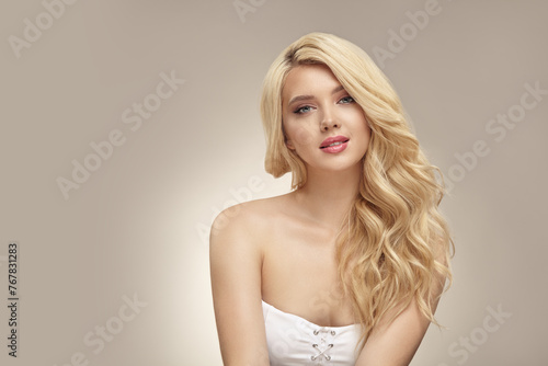 Pretty young blonde woman with nude makeup has a curly long bright hair, close up portrait on beige isolated