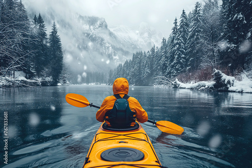 back of a male kayaker kayaking on river in winter with a landscape of mountains and forests in snow photo