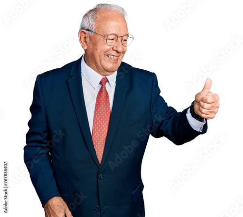 Senior man with grey hair wearing business suit and glasses looking proud, smiling doing thumbs up gesture to the side