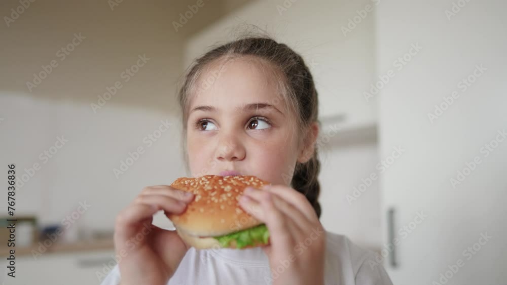 little kid girl eating a hamburger. unhealthy fast food meal proper nutrition concept. child greedily with pleasure bites a big burger in the kitchen at home. kid eats lifestyle fast food close-up little kid girl eating a hamburger. unhealthy fast food meal proper nutrition concept. child greedily with pleasure bites a big burger in the kitchen at home. kid eats lifestyle fast food close-up
