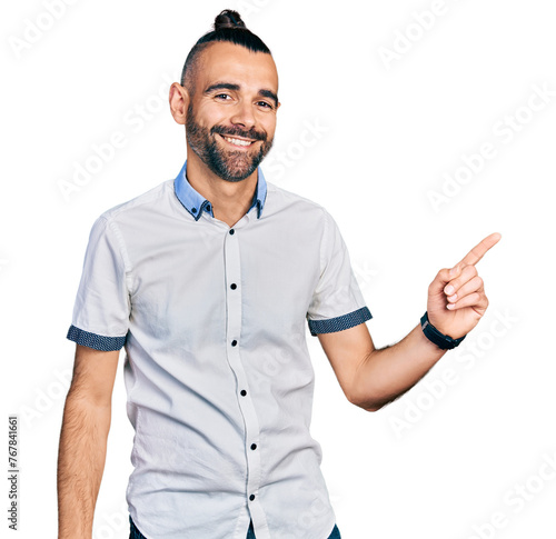 Hispanic man with ponytail wearing casual white shirt with a big smile on face, pointing with hand finger to the side looking at the camera.