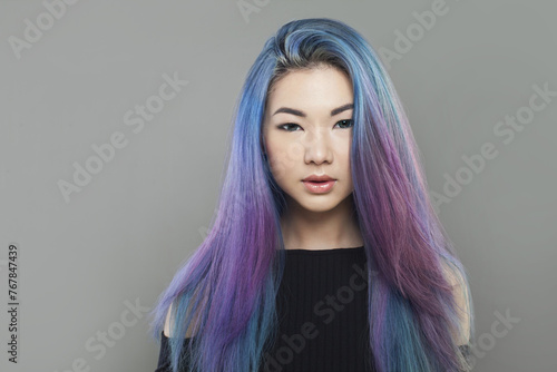 Attractive young asian woman with healthy long colored blue and purple hair on gray background, studio portrait