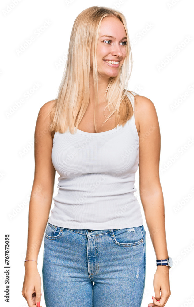 Fototapeta premium Young blonde girl wearing casual style with sleeveless shirt looking away to side with smile on face, natural expression. laughing confident.
