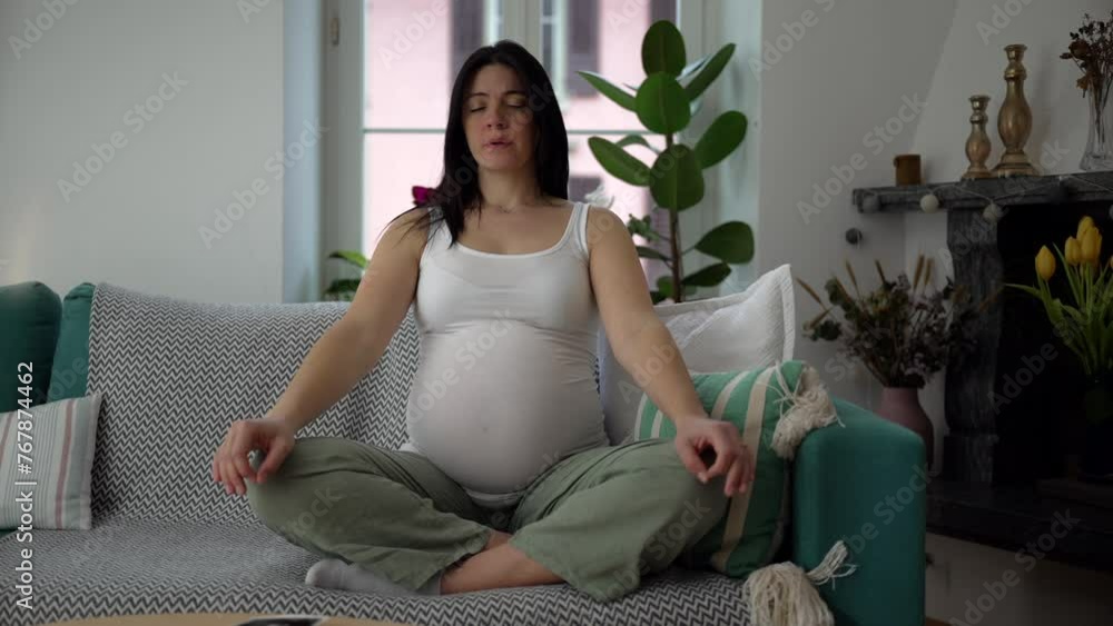 Pregnant woman meditating at home couch with eyes closed in