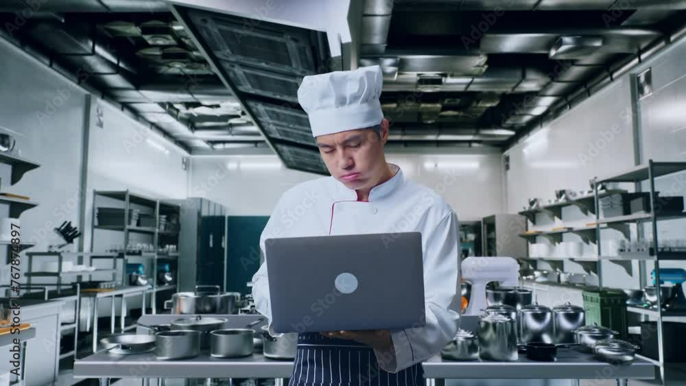 Asian Man Chef Using A Laptop And Having A Headache While Standing In Kitchen Asian Man Chef Using A Laptop And Having A Headache While Standing In Kitchen