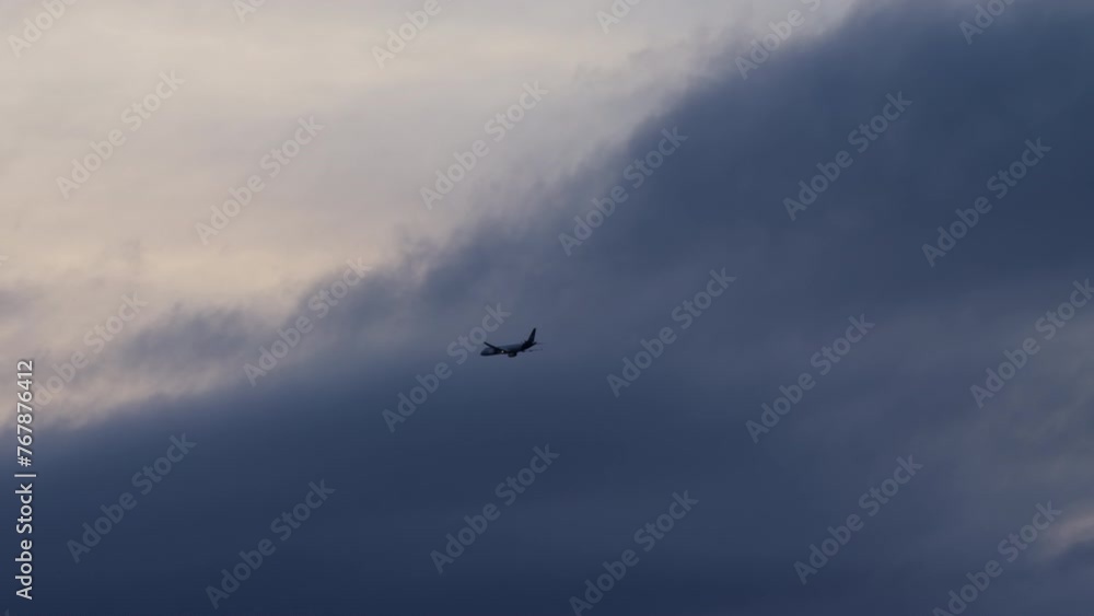 Silhouetted airplane executing a turn and entering a dense formation of dark clouds in the sky Silhouetted airplane executing a turn and entering a dense formation of dark clouds in the sky