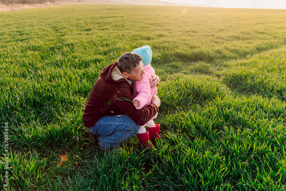 Grandfather and granddaughter hugging in the field with sunshine