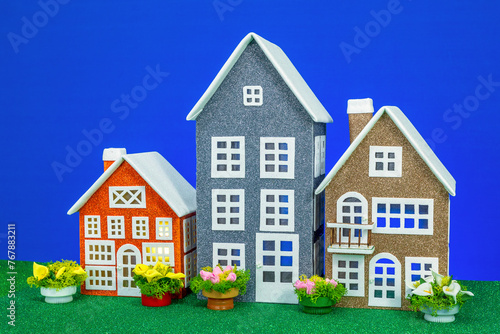 Three toy houses of different sizes with flowers nearby on a blue background