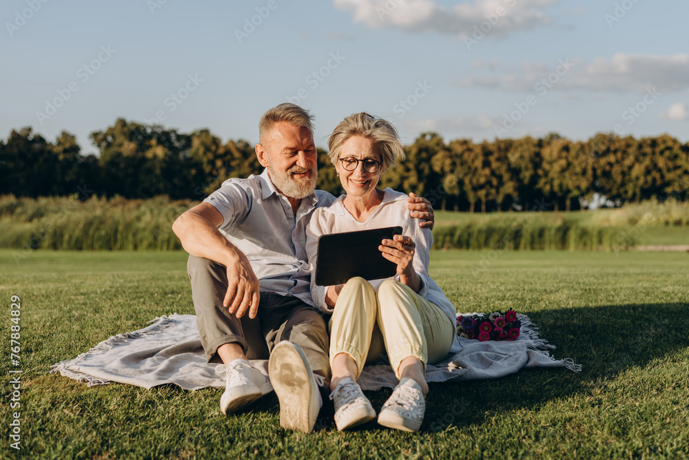 Joyful elder couple relaxing outdoors with digital tablet