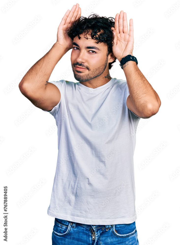 Hispanic young man with beard wearing casual white t shirt doing bunny ears gesture with hands palms looking cynical and skeptical. easter rabbit concept. Hispanic young man with beard wearing casual white t shirt doing bunny ears gesture with hands palms looking cynical and skeptical. easter rabbit concept.