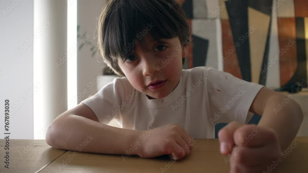 Assertive child hits table surface with hand. 5 year old boy demanding attention while looking at camera, close-up face and fist